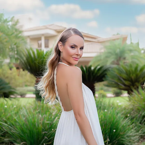 Mulher de vestido branco em jardim, com casarão ao fundo